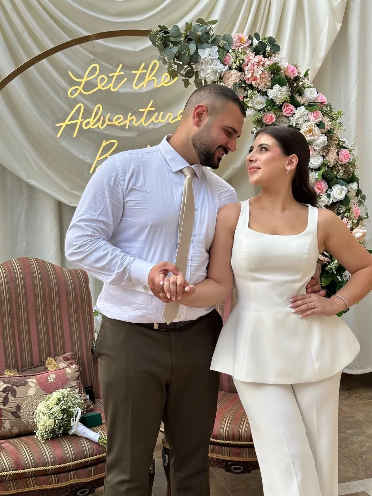 The couple hand in hand under a flower arch