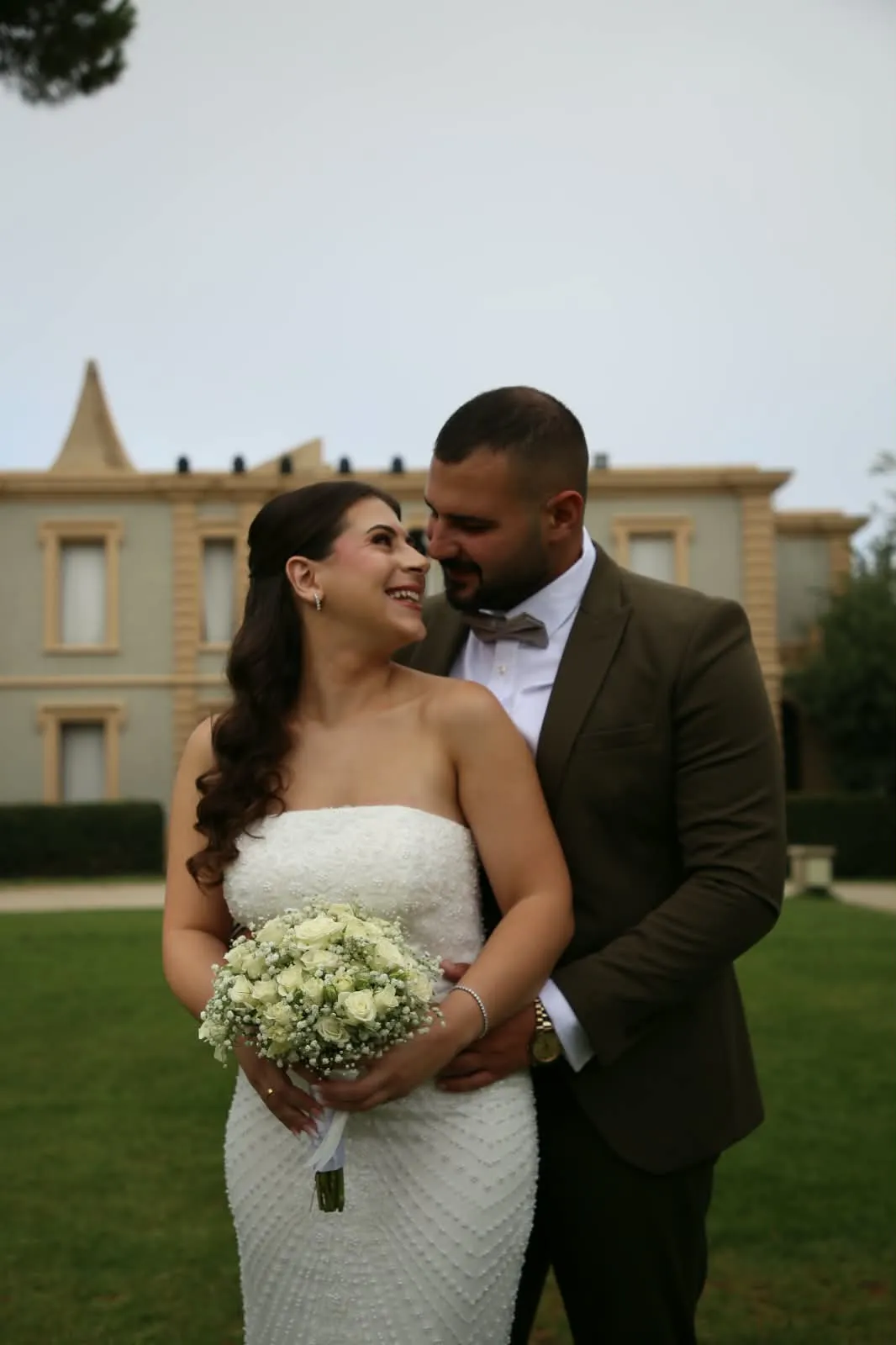 The couple laughing in an embrace, the bride holding white roses